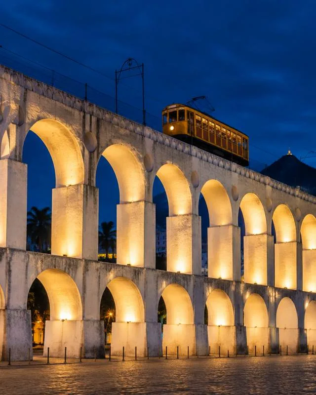 Arcos da Lapa iluminados à noite, com o bondinho passando